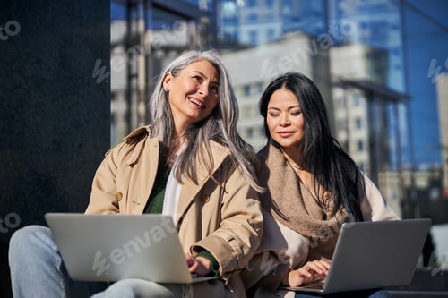 Preview: Two charming women using laptops on the street