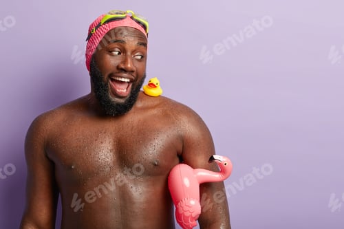Preview: Funny dark skinned father buys swimming accessories for child, looks happily at small rubber ducklin
