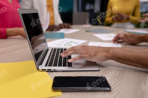 Preview: Cropped hand of hispanic businessman using laptop at conference table during meeting with colleagues
