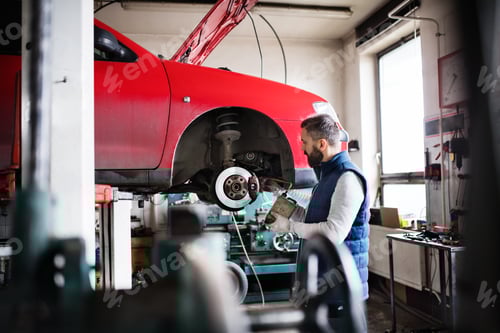 Preview: Man mechanic repairing a car in a garage.