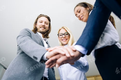 Preview: Young coworkers putting hands together as symbol of unity in the office