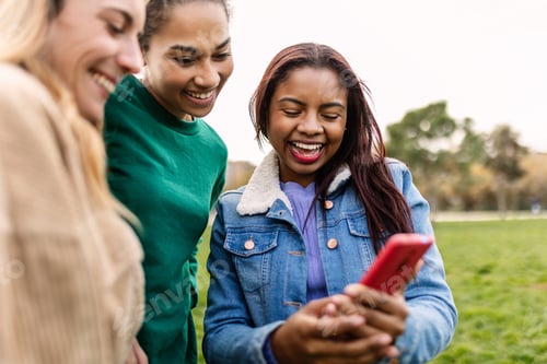 Preview: Three multiracial female friends holding mobile phone outdoor