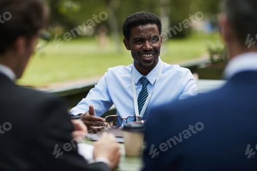 Preview: Young Black Man Smiling While Discussing Business Outdoors with Colleagues