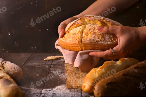 Preview: Loaf of fresh baked wheat bread in woman's hands in sunshine. Rustic day light in dark room.