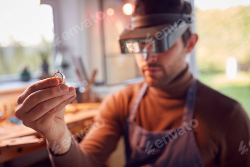 Close Up Of Male Jeweller Looking At Ring Through Headband Magnifiers In Studio