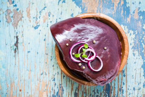 Preview: A piece of raw beef liver in a bowl and spices for cooking on a wooden table. Top view