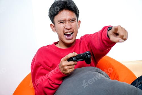 Preview: Excited Young Asian Man Enthusiastically Plays Video Games On Beanbag Using Controller