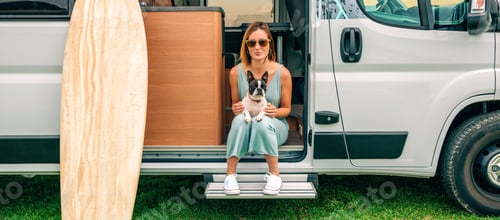 Preview: Woman sitting with her dog at the door of her camper van during a trip
