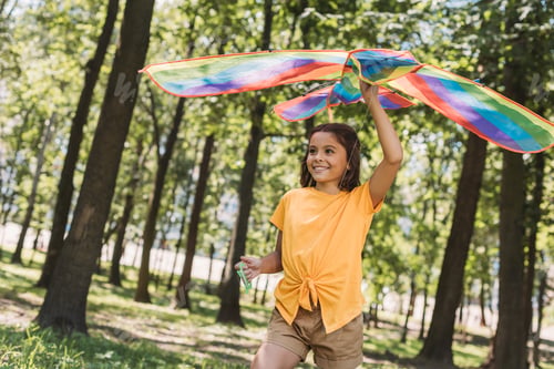 Preview: cute happy kid holding colorful kite and looking away in park