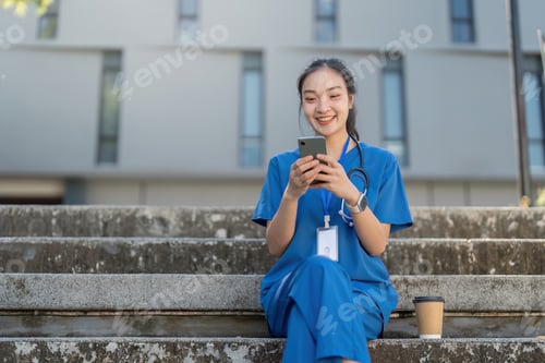Preview: Joyful nurse sitting on steps, smiling while using her smartphone and holding a coffee cup