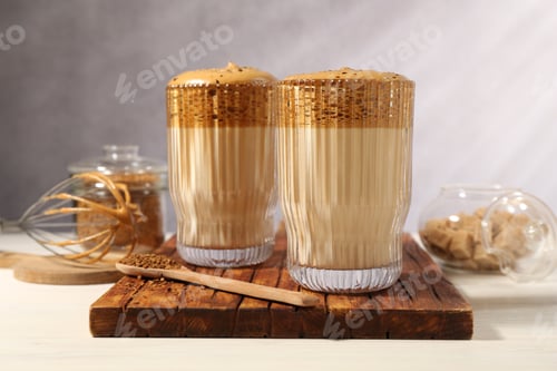 Preview: Delicious dalgona coffee in glasses, whisk, brown sugar and granules on light table, closeup