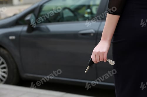 Preview: female hand holding car keys. Back view. female driver standing in front car, outdoors