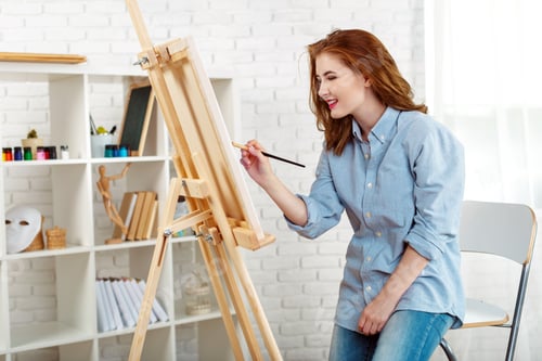 Preview: Woman paints on an easel in a bright studio with art supplies around her