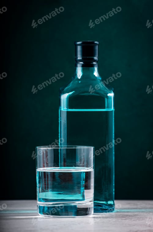 Preview: Dry gin in glass with sapphire blue bottle on dark green background