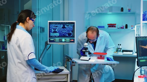 Preview: Researcher using microscope in laboratory while nurse taking notes