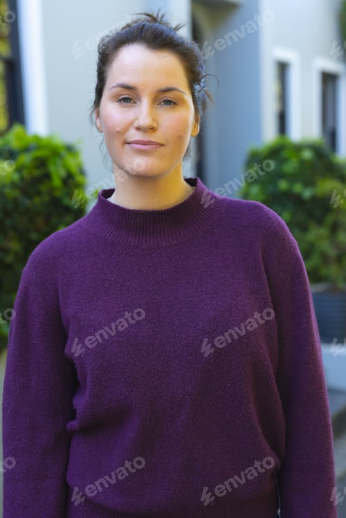 Preview: Happy caucasian woman in purple sweater standing in front of house in garden
