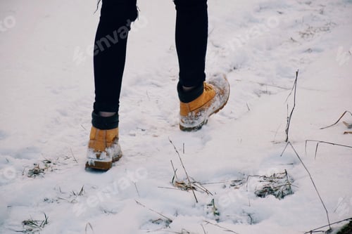 Preview: Feet of a teenage girl in yellow winter boots walking on snow