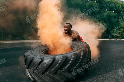 Preview: Handsome muscular man flipping big tire outdoor.