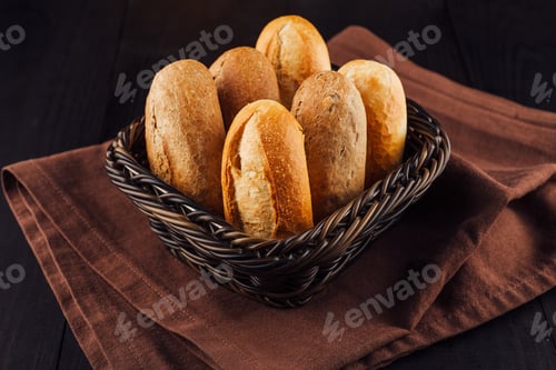 Preview: Freshly baked bread rolls lying in wicker basket on brown napkin