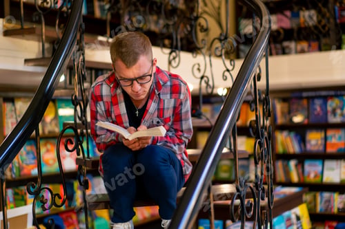 Preview: a man in glasses sits on the stairs in the library carefully reads a book and worries its characters