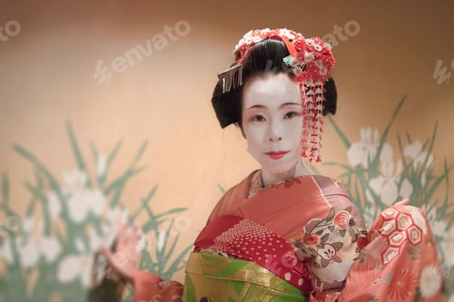Preview: Japanese Maiko or geisha in red kimono against a wall with a pattern of tradional iris flowers.