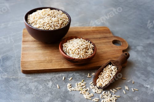 Preview: Wooden bowls filled with raw brown rice sit on a gray surface.