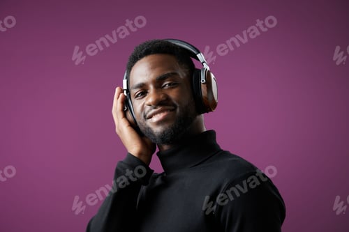 Preview: Young African man enjoying music with headphones, smiling against a purple background, showcasing a