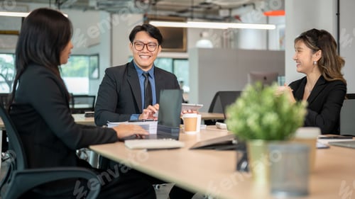 Preview: Happy businessman and woman listening to coworker talking while sitting at wooden table in office.