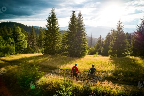 Preview: Two cyclists men resting on the top of hill while riding electric bikes outdoors.