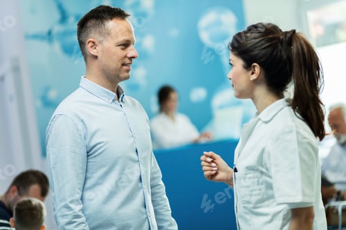 Preview: Smiling patient communicating with female doctor in a hallway at hospital.