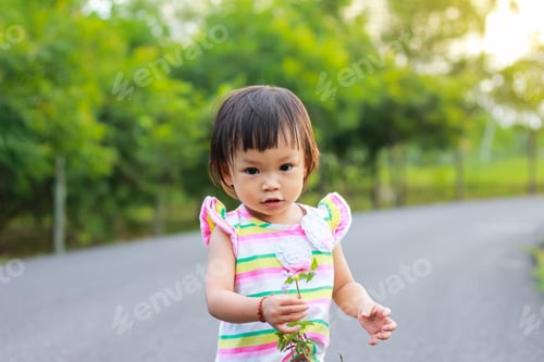 Preview: Happy Asian child girl standing and holding a grass flowers in her hands at the natural park garden