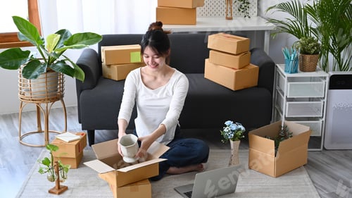 Preview: Happy young business woman small business owner packing product in cardboard box .
