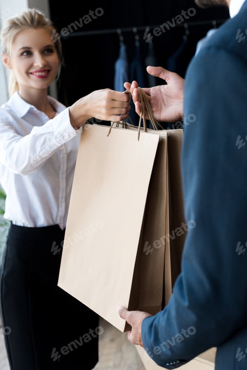Preview: cropped shot of smiling seller giving shopping bags to businessman in boutique