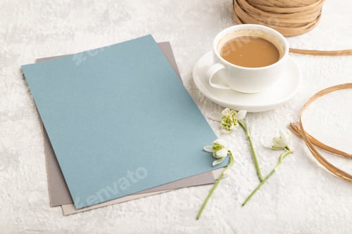 Preview: Blue paper sheet mockup with spring snowdrop galanthus flowers and cup of coffee on gray concrete