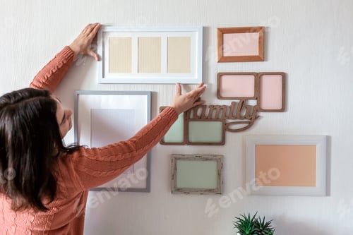 Preview: Girl hanging frame on white wall with set of different empty vertical and horizontal picture frames