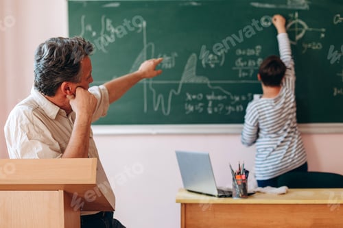Preview: Teacher explain a lesson to student who standing next a blackboard.- Image