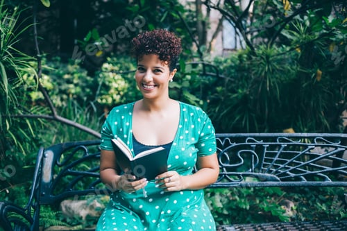 Preview: Content African American chubby woman in casual gown enjoying book at park