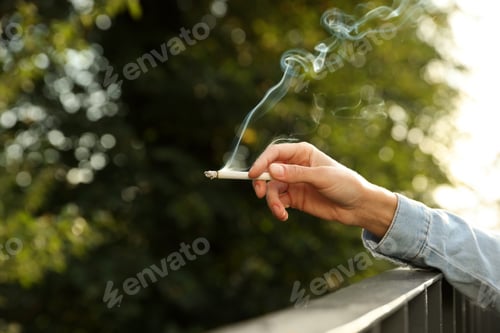Preview: Woman smoking cigarette near railing outdoors, closeup of hand. Space for text