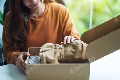 Preview: A woman opening a postal parcel box of clothing at home for delivery and online shopping