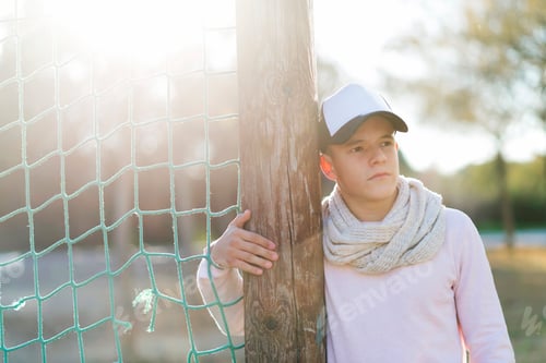 Visualização: Retrato de um adolescente encostado em um mastro de parque, olhando para longe