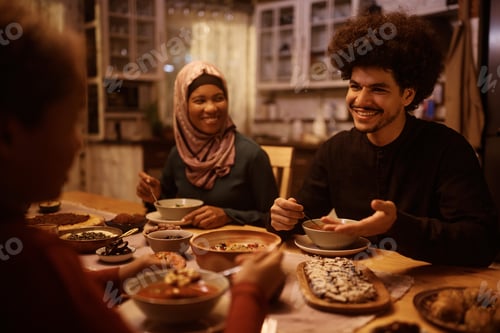 Preview: Happy Middle Eastern man talking to his family while eating dinner at dining table.
