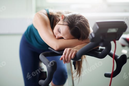 Preview: Exhausted after a workout, a woman takes a moment to rest on a stationary bike.