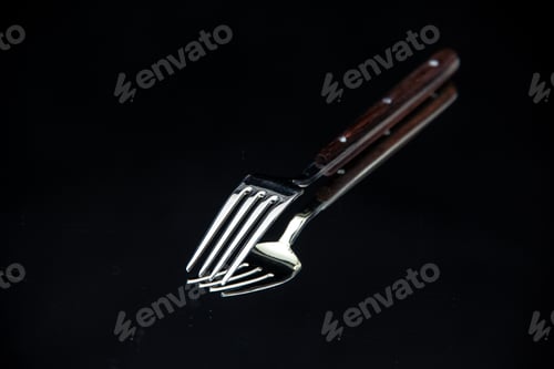 Preview: Front view of elegant shiny metal fork put upside down on black background with free space