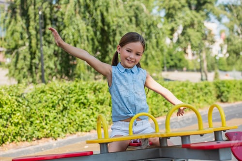 Preview: excited girl looking at camera while riding seesaw with outstretched hands