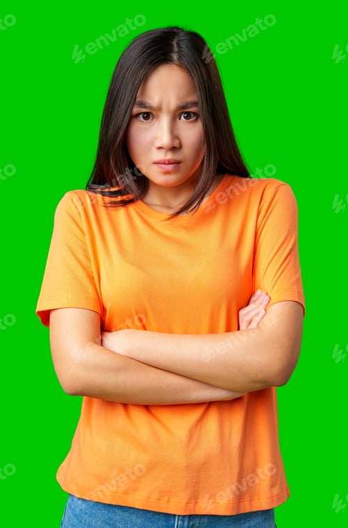 Preview: Young woman expressing frustration while standing against a bright green background in casual attire