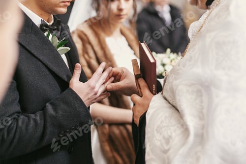 Preview: priest putting on wedding rings on bride and groom hands during holy matrimony in church