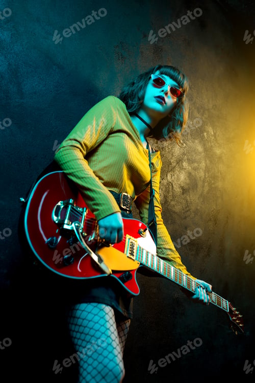 Preview: Beautiful young hipster woman with curly hair with red guitar in neon lights.