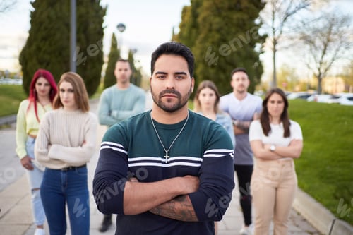 Preview: Latin man looking serious at the camera while standing in front of a group of people.