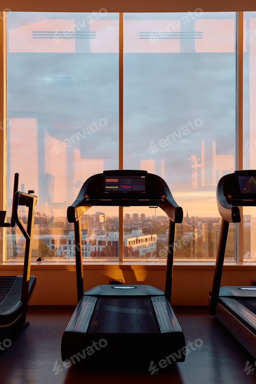 Preview: Interior of health club with treadmill and no people at sunset.