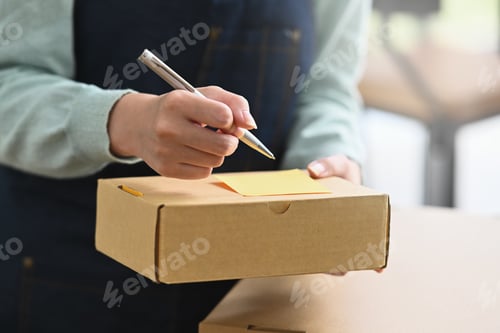 Preview: Close up view female online seller writing address on cardboard box.